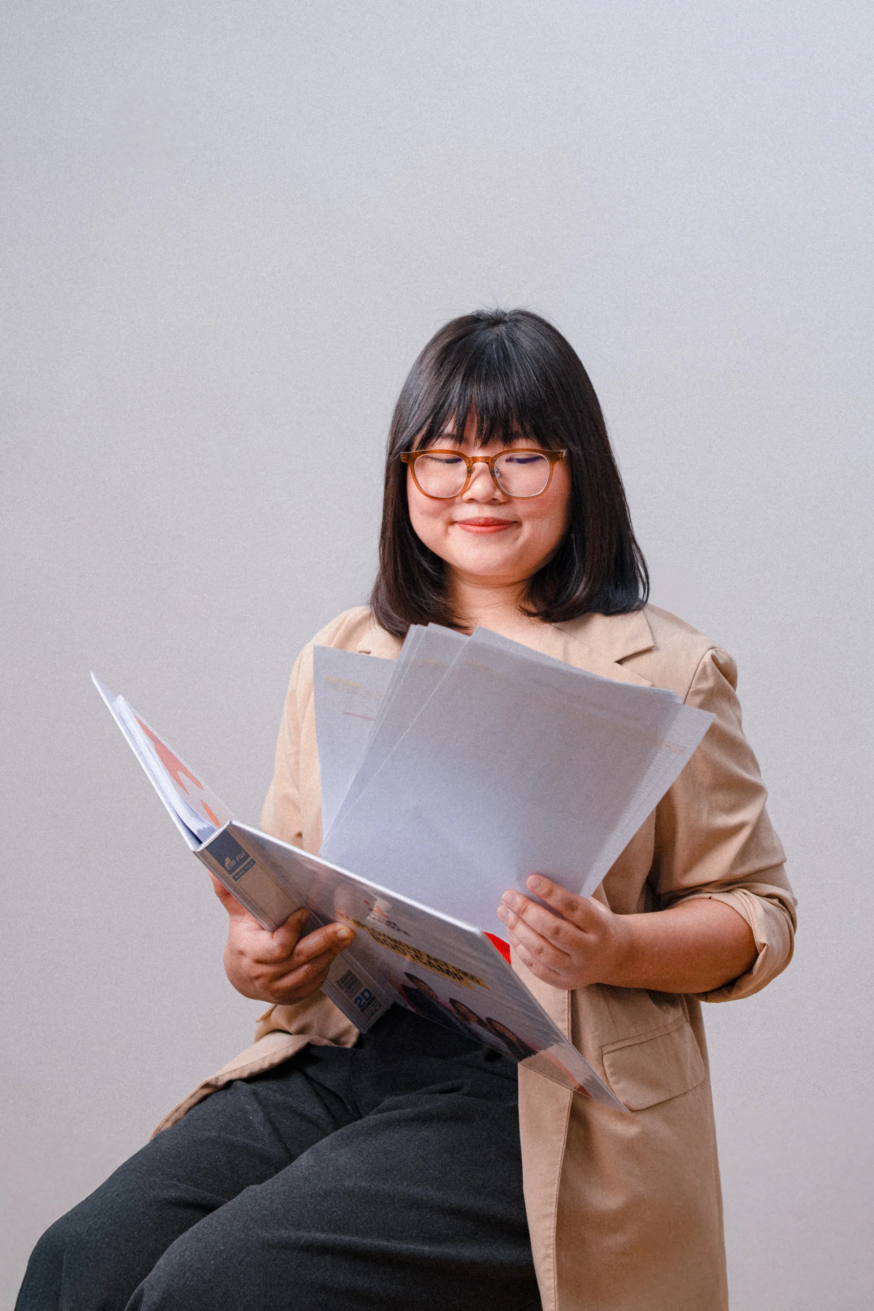 A woman reading documents while seated, wearing a beige blazer and looking focused.