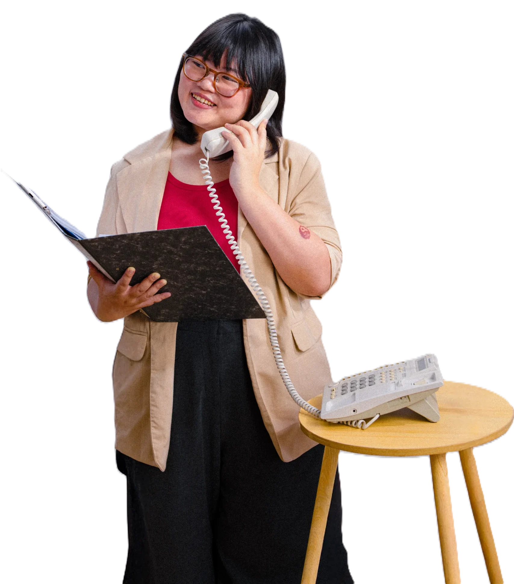 A woman talking on a telephone while holding a clipboard, standing next to a small table.