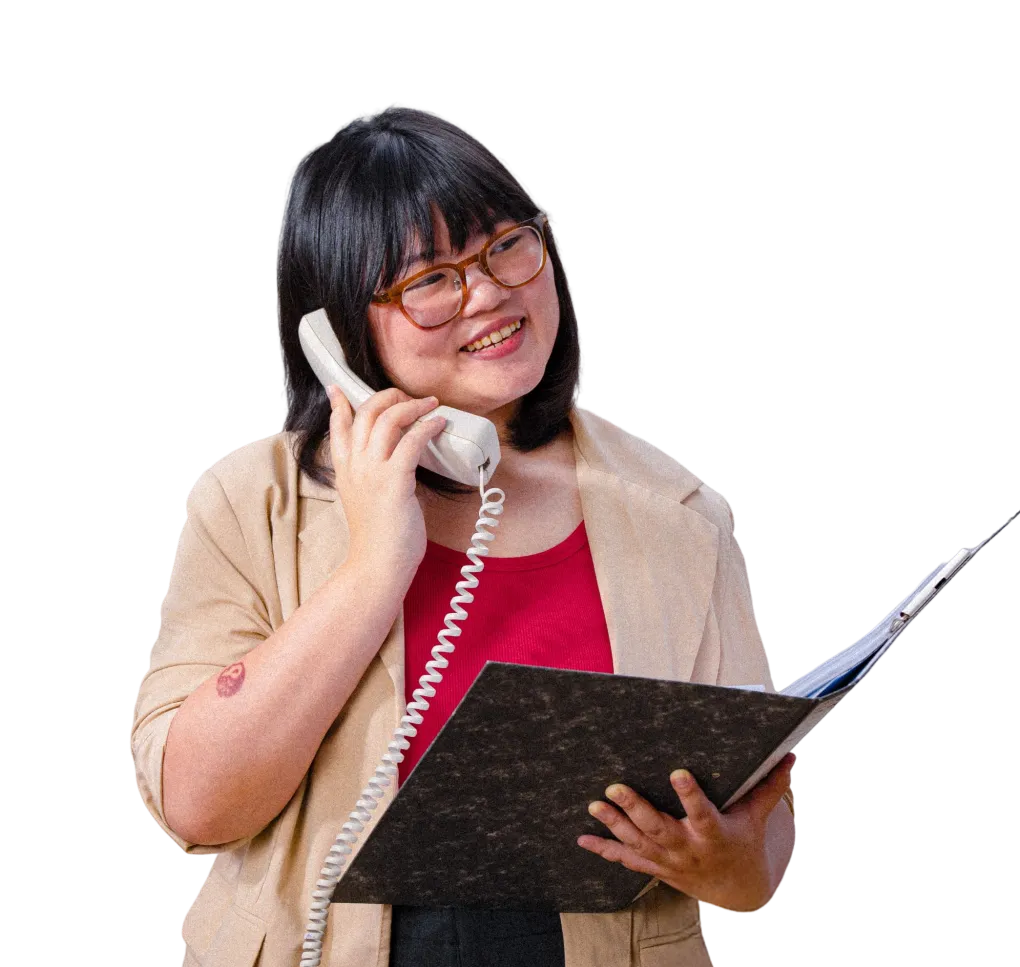 A woman with glasses smiling while talking on a vintage telephone and holding a folder.