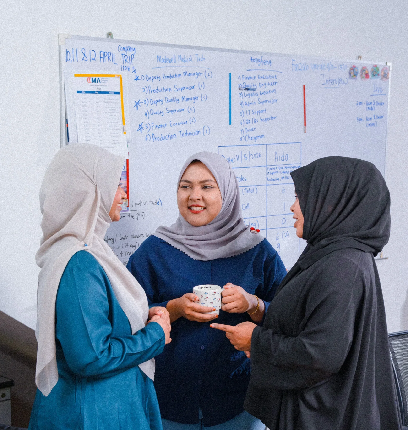Three women in professional attire discussing in front of a whiteboard filled with notes and diagrams.